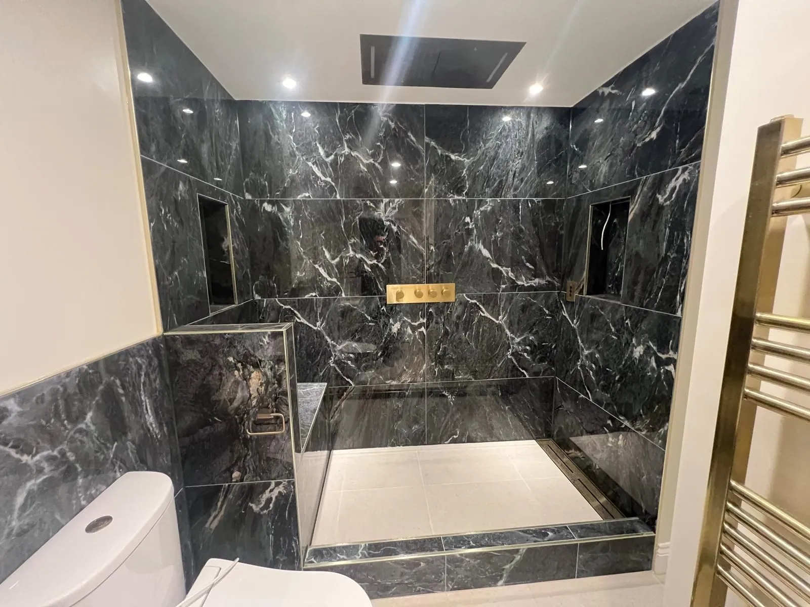 Black marble-effect shower enclosure with brass trims and a heated towel rail