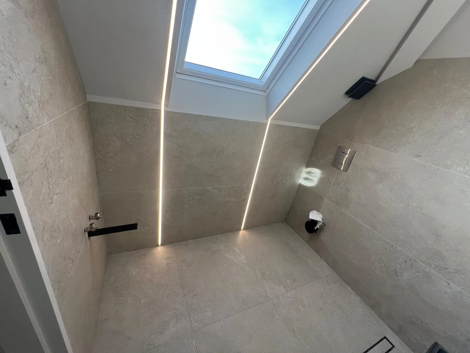 Loft shower room in large-format stone-effect porcelain with LED strips and a skylight